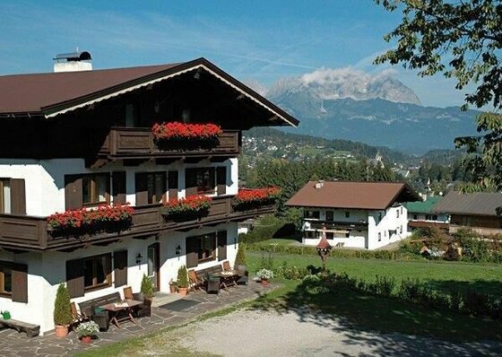 Alpines Gästehaus mit Holzbalkonen und Blumenschmuck vor Bergpanorama.