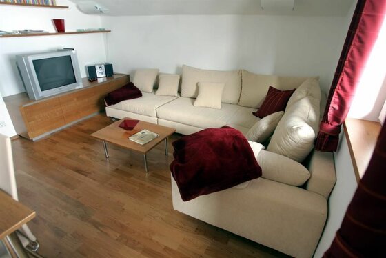 Wohnzimmer Wohnanlage Wurzhöhe Wohnzimmer mit hellem Ecksofa, Holztisch und Fernseher auf einem Sideboard.
