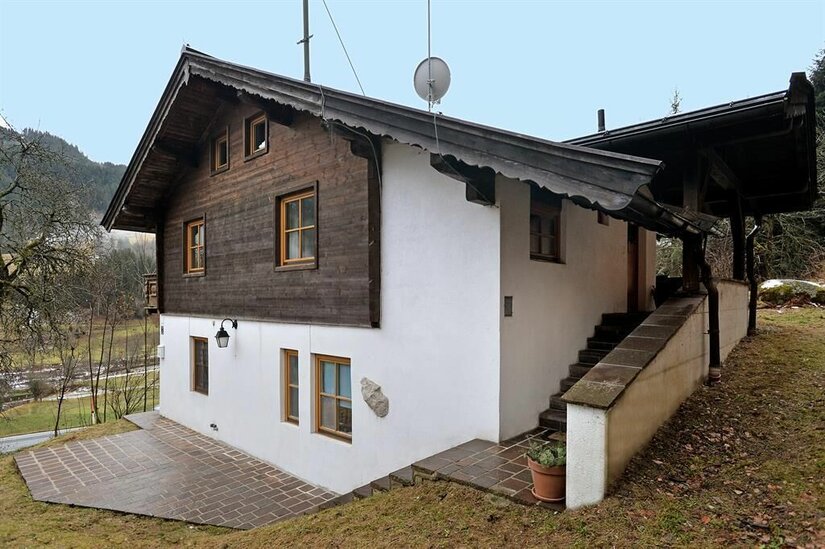 Appartement Holzleitner Jochberg Außenansicht Zweistöckiges Haus mit weißer Fassade im Erdgeschoss und dunkler Holzverkleidung im Obergeschoss.