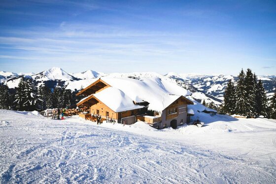 Hochbrunn Alm im Winter Schneebedeckte Almhütte aus Holz in einer alpinen Winterlandschaft mit Bergen im Hintergrund.