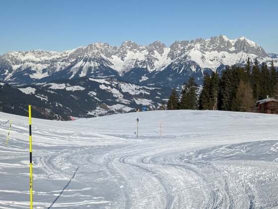 Winterliches Gebirgspanorama Präparierte Skipiste im Vordergrund mit Blick auf ein verschneites Gebirgsmassiv unter blauem Himmel.