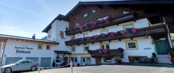 Apartment-Pension Hillebrand Mehrstöckiges Gebäude der Apartment-Pension Hillebrand mit Holzbalkonen und Blumenschmuck unter blauem Himmel.
