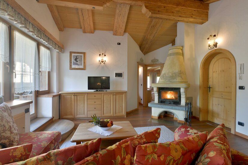 Wohnbereich im Ploderhaus Rustikaler Wohnraum mit Holzbalkendecke, Kaminfeuer, TV und gemusterten Sofas.