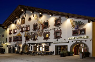Casino Ein traditionelles Gebäude mit bemalten Fassaden und vielen Fenstern. Das Kasino Kitzbühel ist deutlich erkennbar und die Atmosphäre ist einladend.
