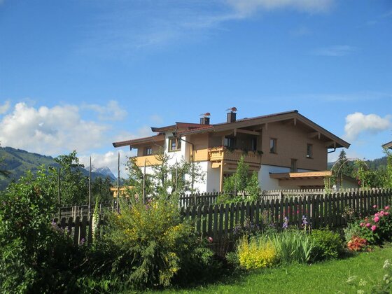 Alpines Wohnhaus mit Holzbalkonen hinter einem Gartenzaun bei blauem Himmel.