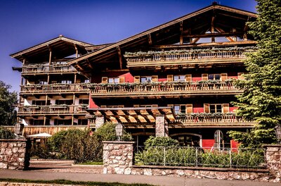 Außenansicht front Hotel Kitzhof Ein schönes Holzhaus im Alpenstil mit mehreren Balkonen. Umgeben von Bäumen und grünen Pflanzen.