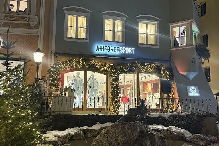 Airforce Sport Store Beleuchtetes Sportgeschäft bei Nacht mit Weihnachtsdekoration und einem Steinbrunnen im Vordergrund.