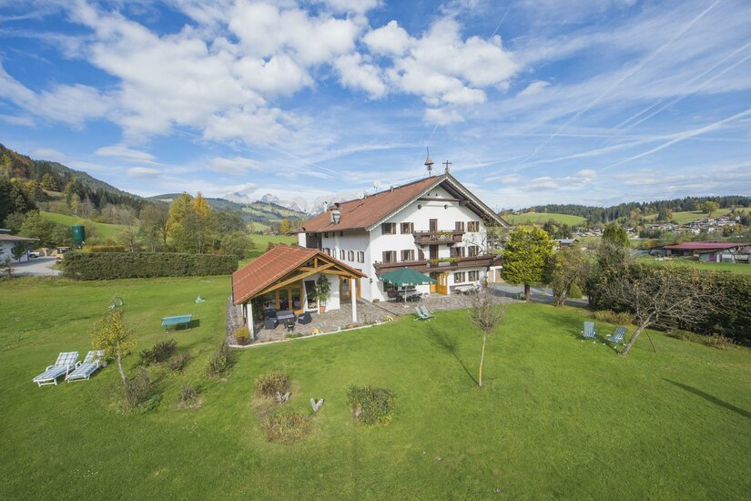 Ein weißes Landhaus mit rotem Dach und großer grüner Wiese unter blauem Himmel.