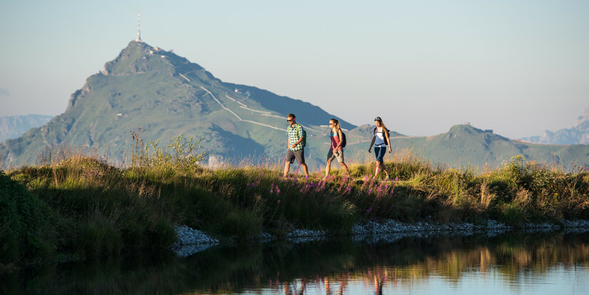 3 people walking along a lake