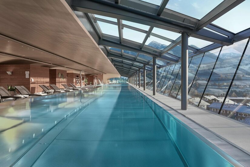 Hallenbad im Lebenberg Schlosshotel Langes Hallenbad mit Glasfront, Liegestühlen und Blick auf die verschneiten Alpen.