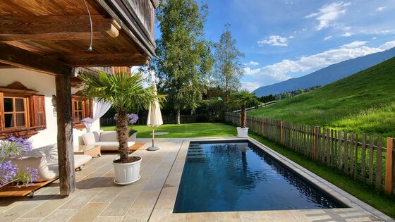 Garten mit Pool Außenpool auf einer Steinterrasse vor einem Holzchalet mit Blick auf grüne Hügel.