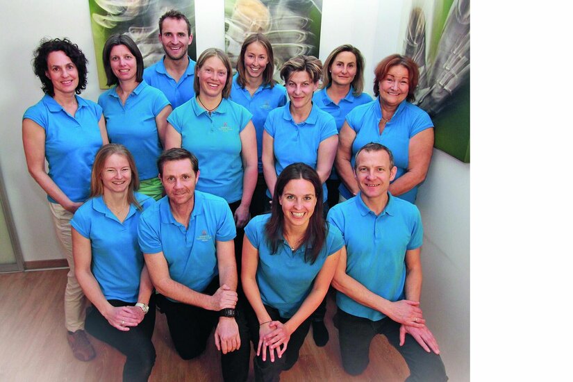 Ein elfköpfiges Team in blauen Poloshirts posiert in einem hellen Innenraum für ein Gruppenfoto.