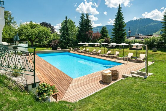 Außenpool am Hotel Tennerhof Außenpool mit Holzumrandung, Liegestühlen und Sonnenschirmen vor einer Bergkulisse.