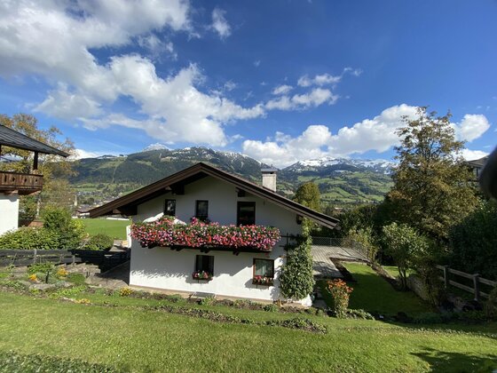 Ausblick Sommer Haus Kolb Alpines Wohnhaus mit blumengeschmücktem Balkon vor schneebedeckten Bergen unter blauem Himmel.