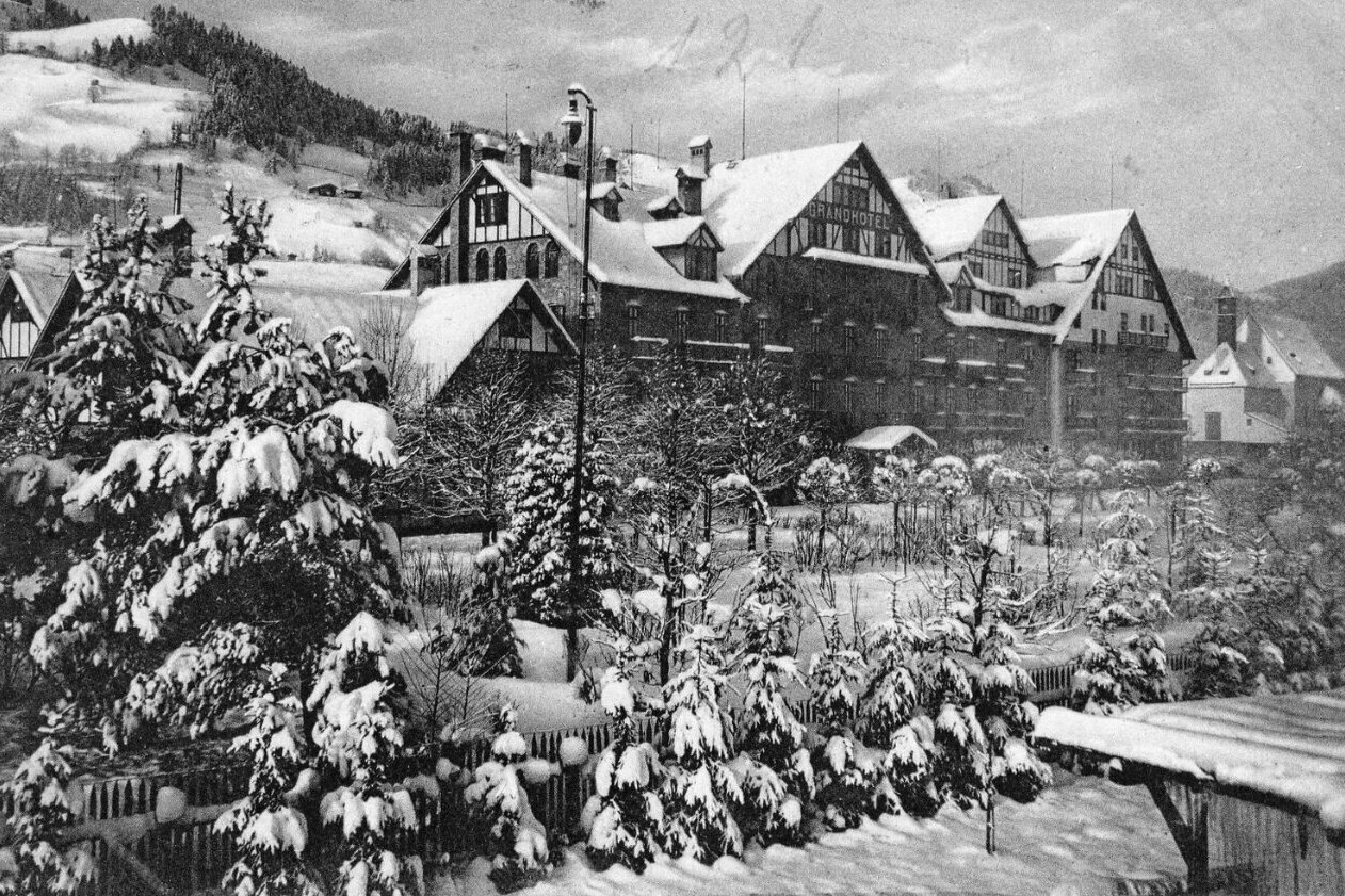 Schwarz-weiß-Foto des Grand Hotels Kitzbühel im Winter mit schneebedeckten Bäumen und Sträuchern
