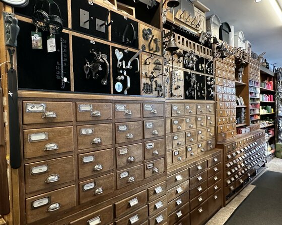 Eisenwarenhandlung Salvenmoser Innenansicht eines Ladens mit hohen Holzschränken voller kleiner Schubladen und Metallbeschlägen an der Wand.