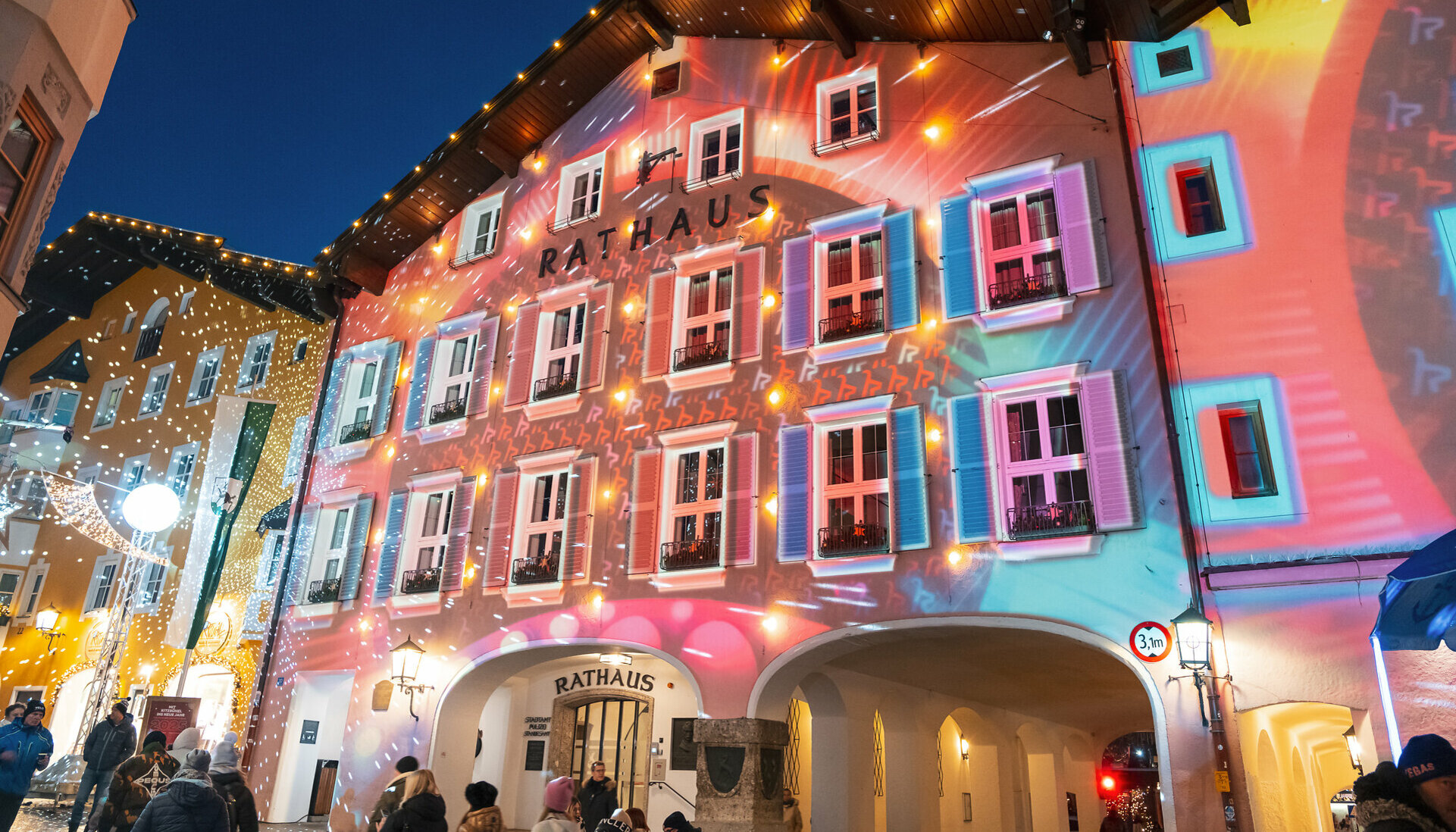 Die Fassade des Rathauses in Kitzbühel erstrahlt in bunten Lichtern und Projektionen während einer festlichen Veranstaltung.