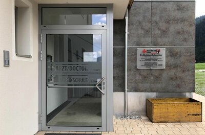 Eingang Dr. Schwentner Eingangsbereich einer Arztpraxis mit Glastür und Hinweisschild an einer grauen Fassade.