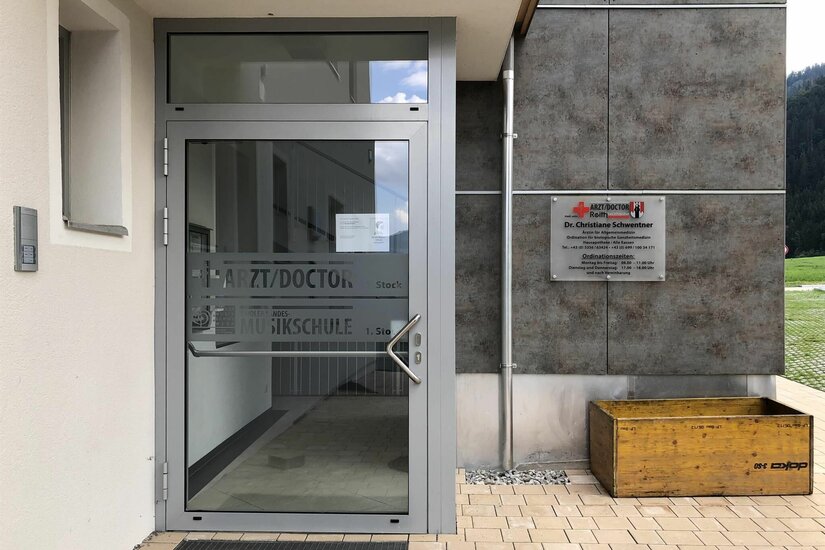 Eingang Dr. Schwentner Eingangsbereich einer Arztpraxis mit Glastür und Hinweisschild an einer grauen Fassade.
