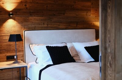 Bedroom 2 Kingsize Bed Modernes Doppelbett vor einer Wand aus dunklem Altholz mit Nachttischlampe.