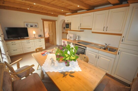 Auracherhof Appartment Wohnküche Helle Wohnküche mit Holztisch, Küchenzeile, Fernseher und Holzdecke.