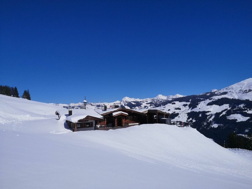 Holzhütte in einer verschneiten Gebirgslandschaft unter blauem Himmel.