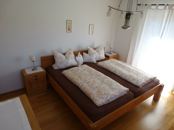 Schlafzimmer in der Sommerau Ein Doppelbett aus Holz mit brauner Bettwäsche und gemusterten Decken in einem hellen Zimmer.