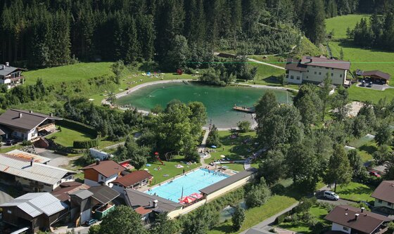 Ein malerischer Ort mit einem klaren See und einem Schwimmbecken. Umgeben von grünen Wäldern und gemütlichen Häusern.