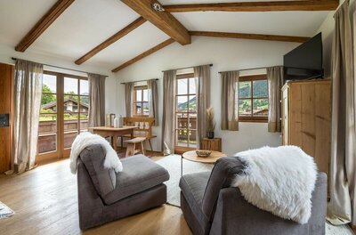 Wohnbereich eines Apartments mit zwei Sesseln, Holztisch, Eckbank und Sichtbalken an der Decke.