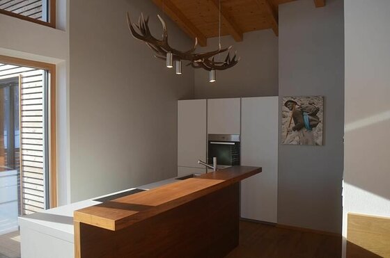 Küche im Apartment Hofer Moderne Küche mit Holztheke, Geweih-Leuchte und weißer Schrankwand unter einer Holzdecke.