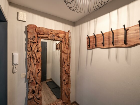 Flur mit großem Altholzspiegel und einer Wandgarderobe aus Holz mit schwarzen Metallhaken.