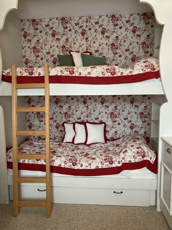 Etagenbett in Ferienwohnung Weißes Etagenbett mit Blumenmuster-Bettwäsche und Holzleiter in einer Nische.
