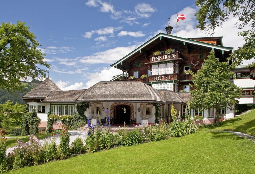 Hotel Tennerhof Außenansicht Außenansicht des Hotel Tennerhof mit Holzfassade, Blumengarten und österreichischer Flagge unter blauem Himmel.