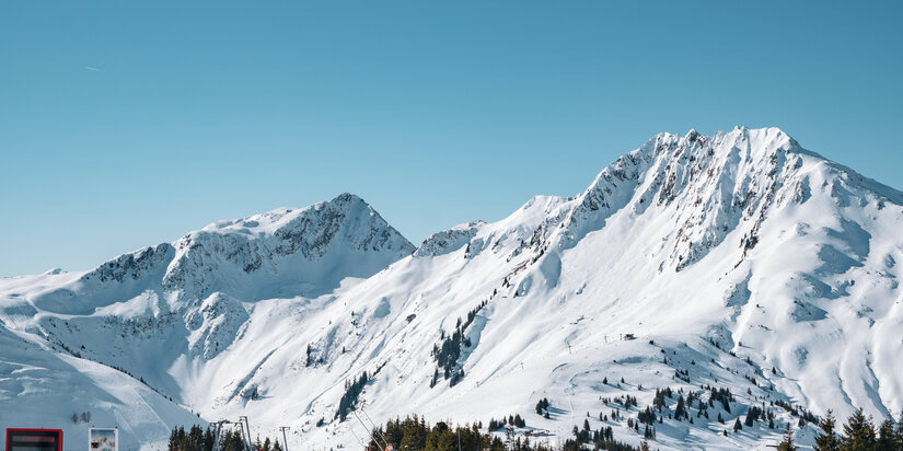 At the Kleiner Rettenstein in the Kitzbühel ski area, snow-capped mountains rise against a bright blue sky.