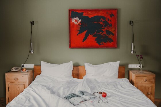 Zimmer im Hotel Seebichl Doppelbett mit weißer Bettwäsche vor grüner Wand mit rotem Gemälde und Holz-Nachttischen.