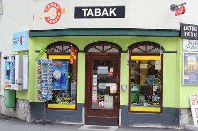 Trafik Sevignani Außenansicht einer Tabak-Trafik mit hellgrüner Fassade, Postkartenständer und Verkaufsautomaten.