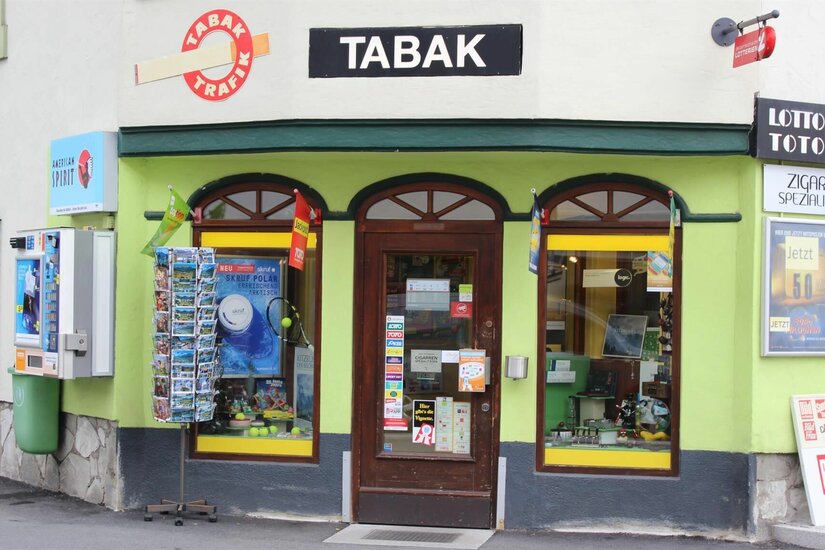Trafik Sevignani Außenansicht einer Tabak-Trafik mit hellgrüner Fassade, Postkartenständer und Verkaufsautomaten.