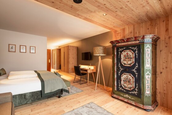 Modernes Hotelzimmer mit Doppelbett, Schreibtisch und einem bemalten Bauernschrank aus Holz.