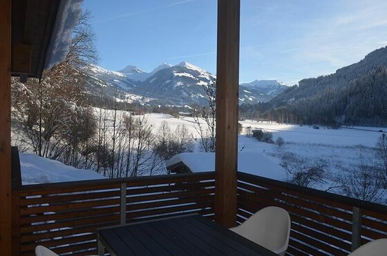 Ausblick vom Apartment Hofer Manfred Blick von einem Holz-Balkon auf ein verschneites Tal und schneebedeckte Berggipfel unter blauem Himmel.