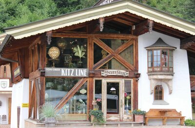 Fassade eines alpinen Gebäudes mit Holzgebälk, großen Schaufenstern und einem kleinen Erker.