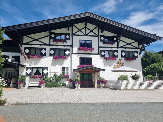 Hotel Zimmermann Garni Vorderansicht des Hotel Zimmermann mit weißer Fassade, dunklem Holzgebälk und Blumenkästen unter blauem Himmel.