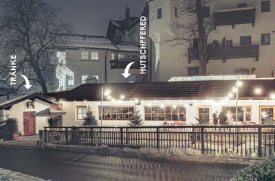 Hutschpferd Ein gemütliches Restaurant bei Nacht, beleuchtet von warmen Lichtern. Im Hintergrund sind einige Häuser und Bäume zu sehen.