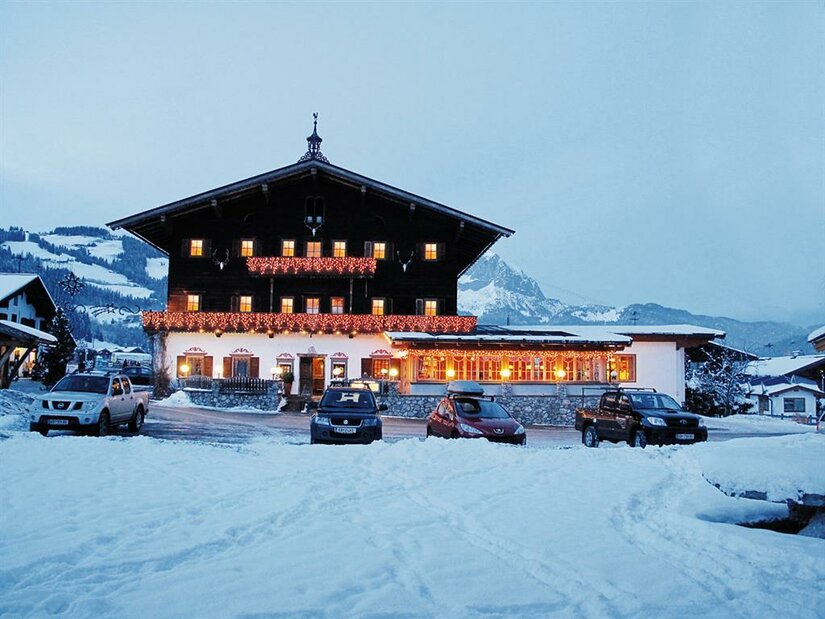 Landgasthof Reitherwirt im Winter Ein beleuchteter Landgasthof in Holzbauweise bei Dämmerung in einer verschneiten Berglandschaft mit parkenden Autos.