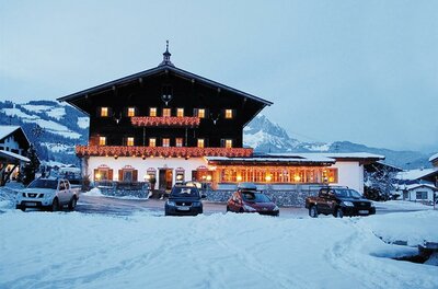 Landgasthof Reitherwirt im Winter Ein beleuchteter Landgasthof in Holzbauweise bei Dämmerung in einer verschneiten Berglandschaft mit parkenden Autos.
