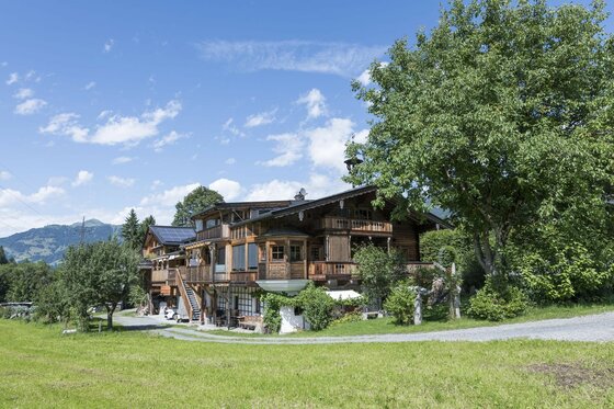 Apartment Nussbaum Außenansicht Mehrstöckiges Holzhaus mit Balkonen auf einer grünen Wiese unter blauem Himmel.
