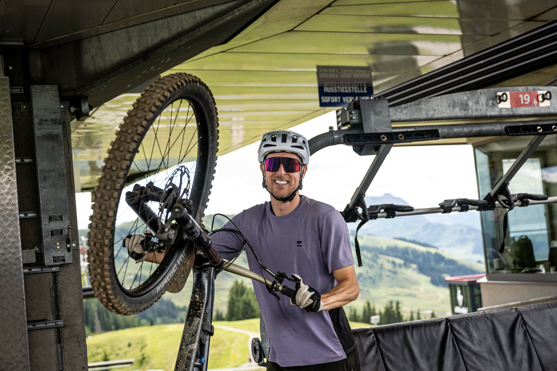 Ein Mountainbiker nimmt sein Fahrrad an einer Liftstation der 360 Flow Trails Kitzbühel vom Bike-Lift, lächelnd und bereit für die nächste Abfahrt.