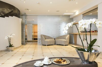 Moderner Wellness-Ruheraum mit zwei Sesseln, hellen Fliesen und Orchideen im Vordergrund.