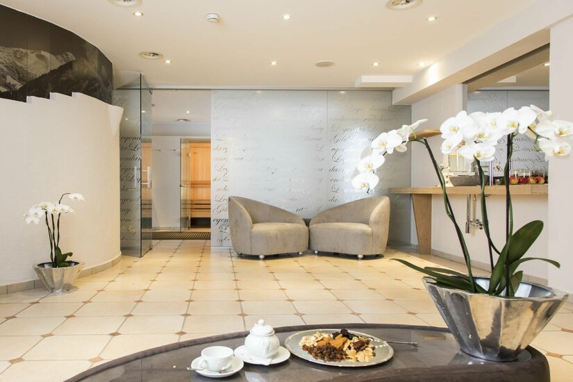 Wellnessbereich im Hotel Reisch Moderner Wellness-Ruheraum mit zwei Sesseln, hellen Fliesen und Orchideen im Vordergrund.