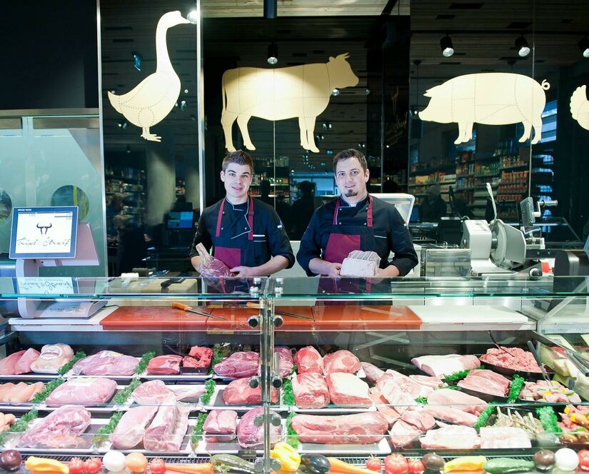 Zwei Metzger hinter einer Verkaufstheke mit verschiedenen Fleischsorten.