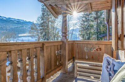 Balkon im Kitz Hills Chalet Holzbalkon eines Chalets mit Blick auf verschneite Berge und Wälder bei Sonnenschein.